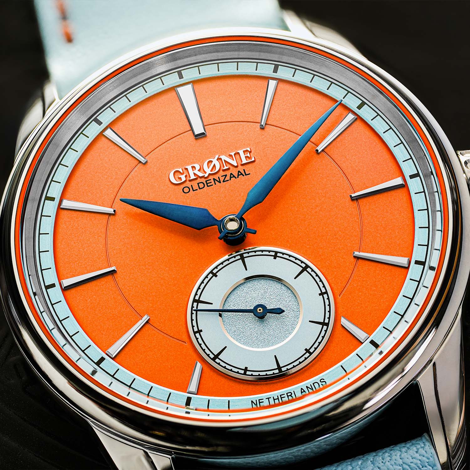 Macro of the Quirky Grøne Oldenzaal Horologium dial, vivid Dutch-orange centre with a light-blue chapter ring, blued hands and a silvered small-seconds sub-dial reading Grøne Oldenzaal Netherlands