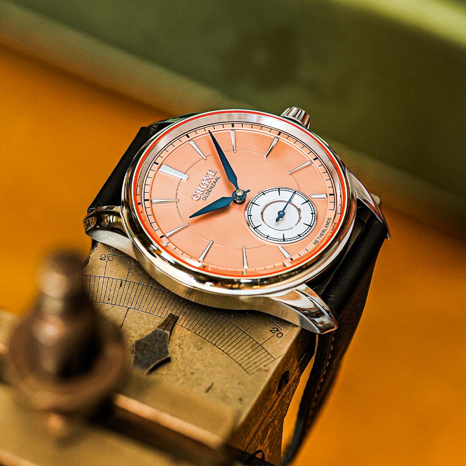 The Classic Grøne Oldenzaal Horologium at a three-quarter angle on a bench, showing the polished steel case, downward-curving stepped lugs and the salmon sunray dial