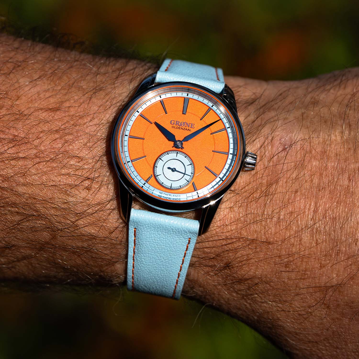 The Quirky Grøne Oldenzaal Horologium on the wrist, orange dial and light-blue leather strap with orange stitching seen in daylight
