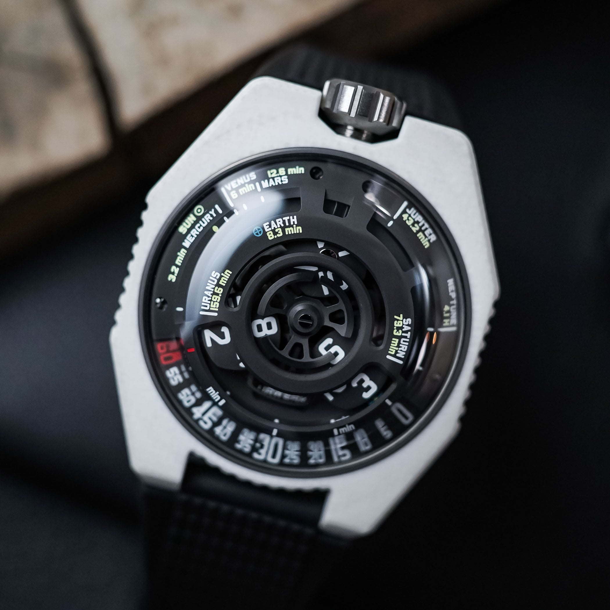 Dial macro of the Urwerk UR-100V Lightspeed Ceramic, the black satellite hour carousel at centre with the planetary light-time scale reading Sun, Mercury, Venus, Mars, Earth 8.3 min, Jupiter, Saturn, Uranus and Neptune, and the red-tipped minute track below
