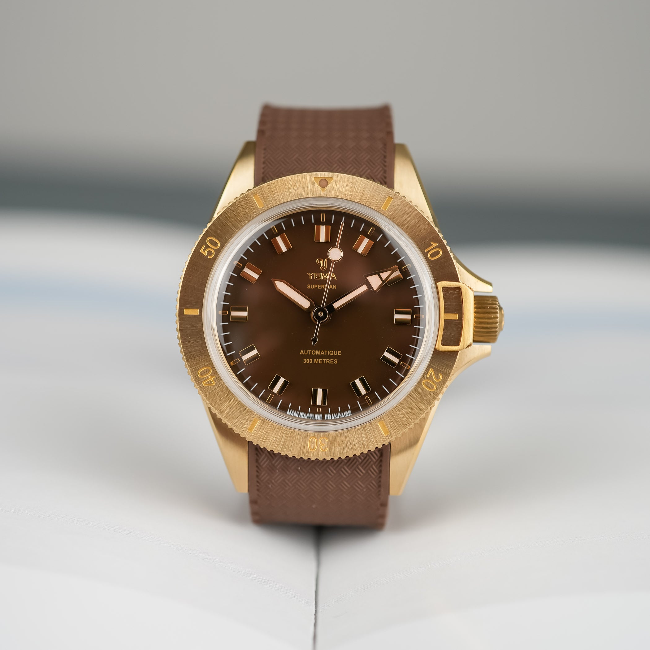 Dial macro of the Yema Superman Bronze CMM.10, glossy brown dial with gilt applied markers, gilt diamond-cut hands and the Manufacture Française text at the base of the dial