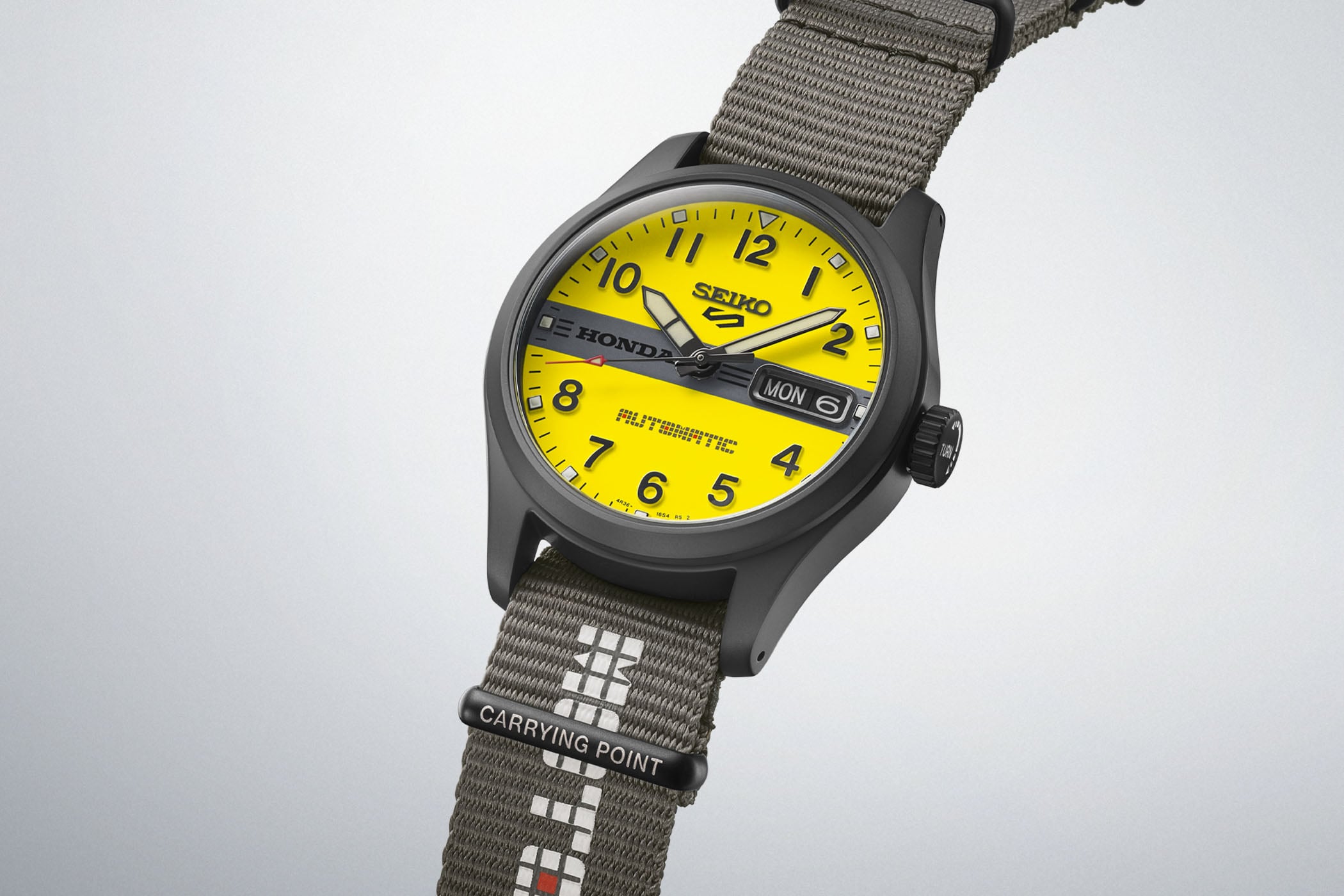 Seiko 5 Sports x Honda Motocompo HDB010 with a bright yellow field dial, a black Honda bar across the centre and a black hard-coated case, on a grey nylon strap with a Carrying Point keeper