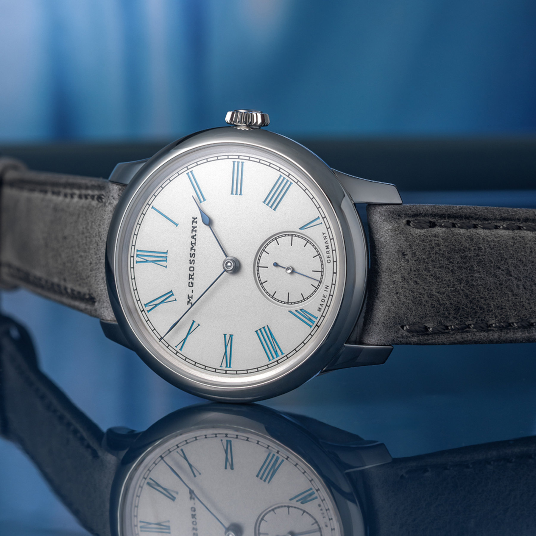 The Moritz Grossmann Tefnut 36 at an angle on its grey kudu strap, showing the polished three-part steel case, flat winding crown and turquoise-accented silvered dial