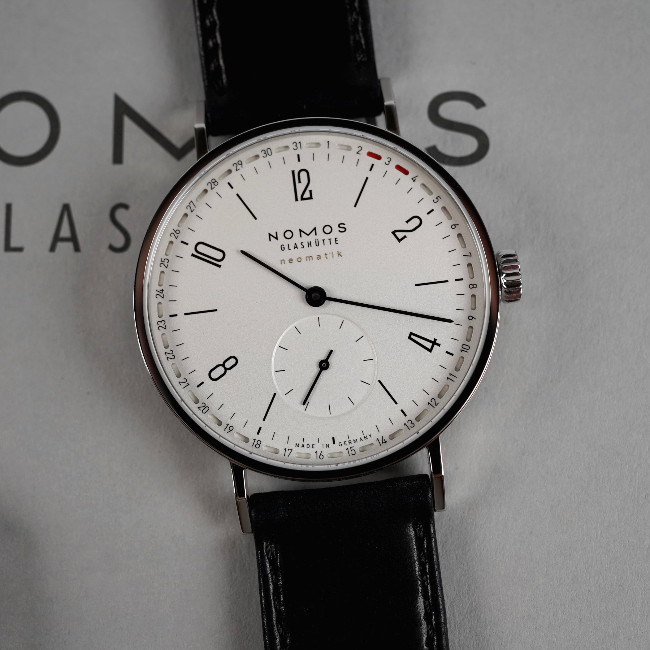 Top-down macro of the silver-dial Nomos Tangente Neomatik 38 Update, reference 147, black printing, a snailed small seconds at 6 and the peripheral date ring picking out the 2nd and 3rd in red