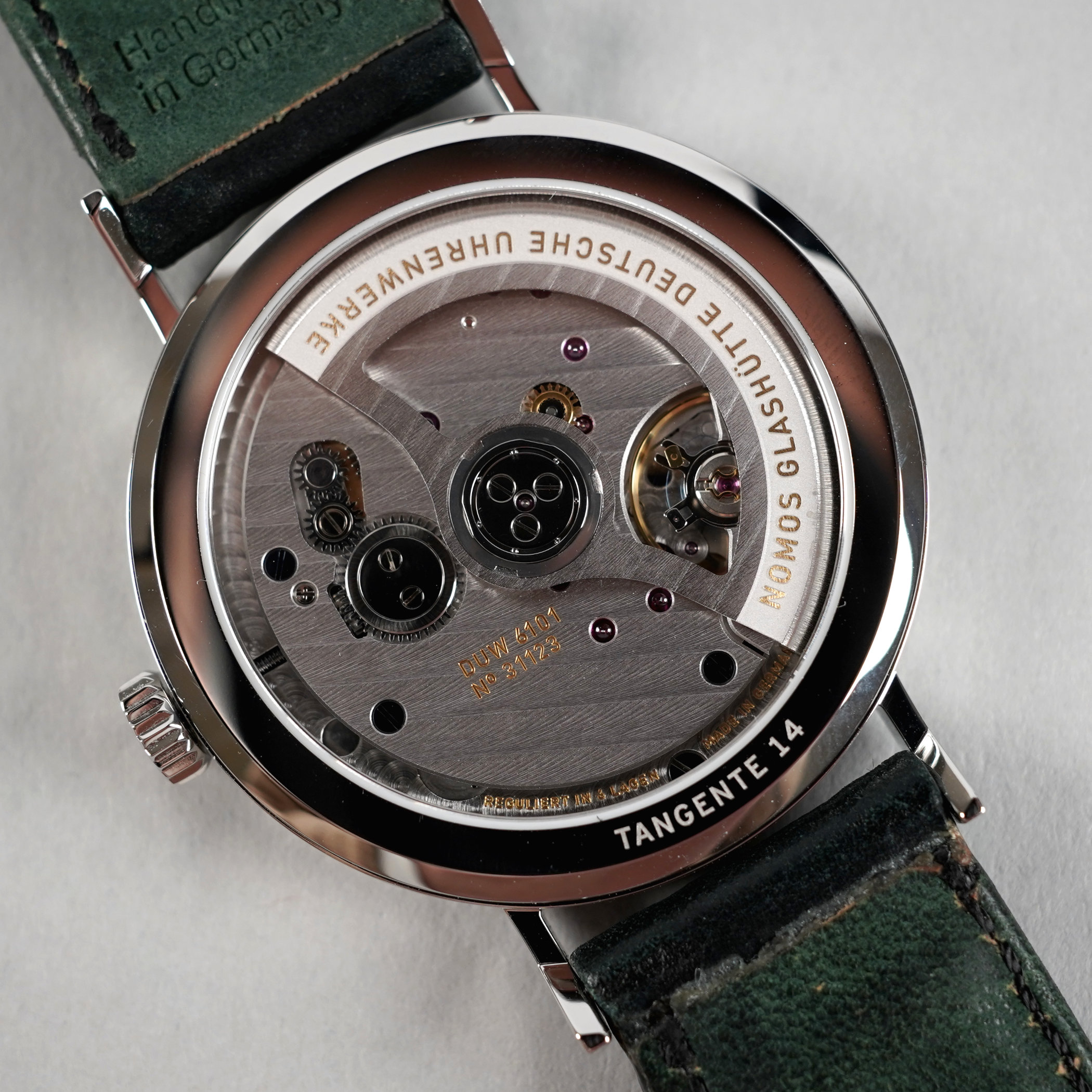 Sapphire caseback of a Nomos Tangente showing the automatic DUW 6101, its Glashütte three-quarter plate with striping, dark screws and the gold DUW 6101 and serial engraving, on a green suede strap
