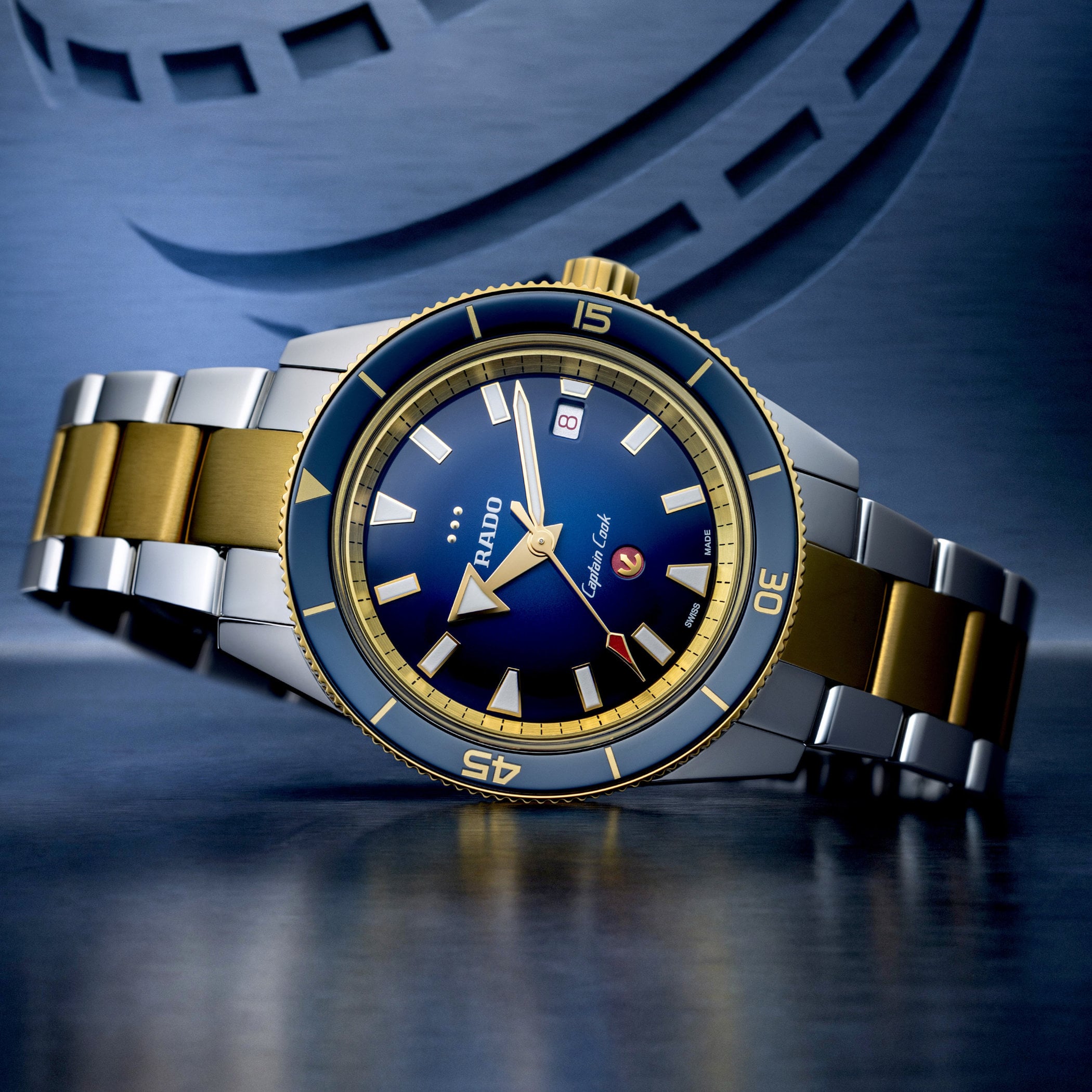 The Rado Captain Cook x European Cricket on its two-tone steel bracelet with yellow gold PVD centre links, the blue gradient dial showing the three gold stump markers and the red cricket-ball anchor