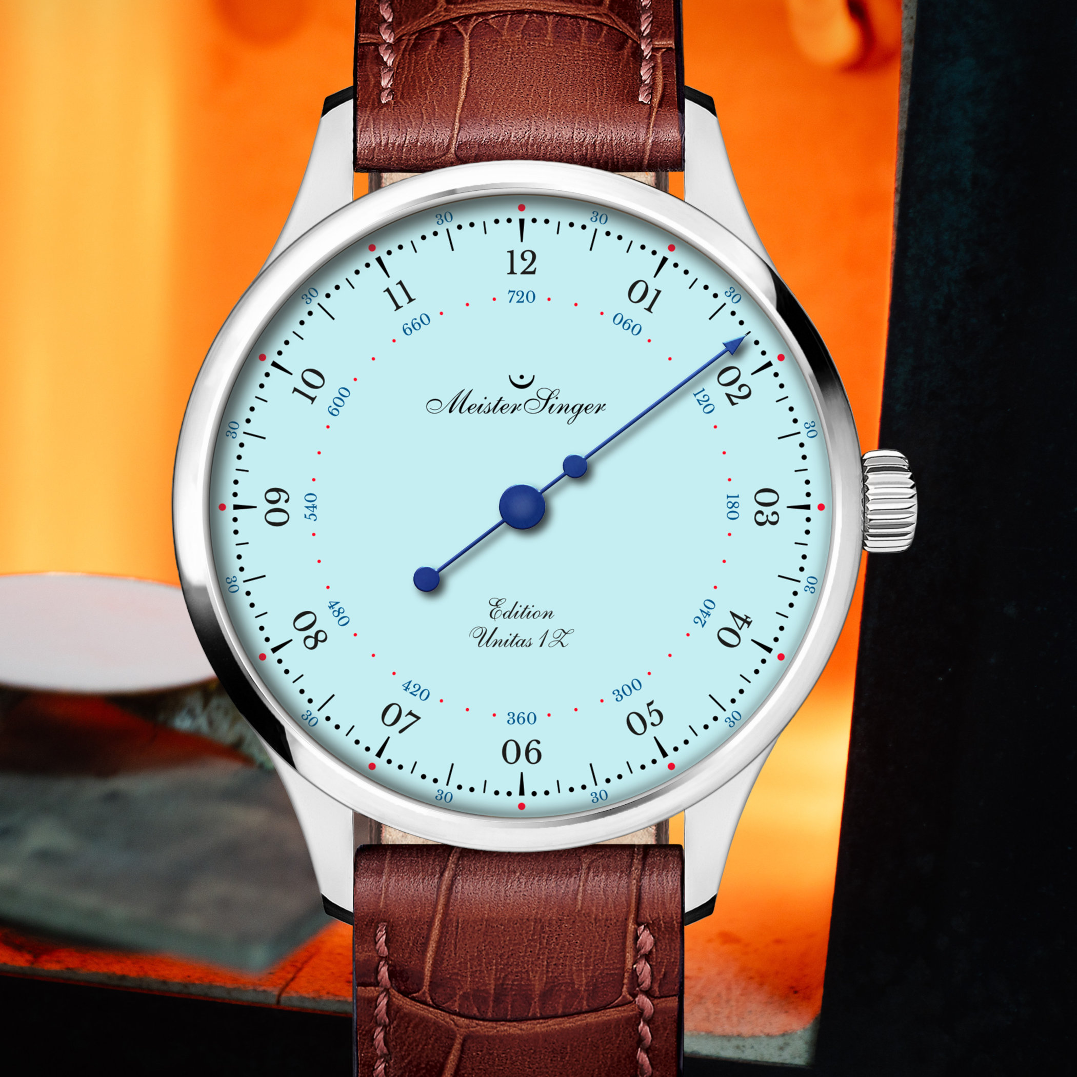 Front macro of the MeisterSinger Edition Unitas 1Z Blue, the light-blue grand feu enamel dial with black hour numerals, red minute dots and a single blue steel hand, shot against an orange background
