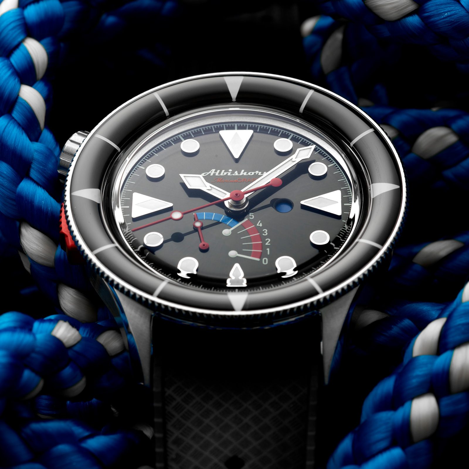 Dial macro of the black Classic Marinagraph resting in coiled blue-and-white sailing rope, showing the applied triangular and circular markers, the blue-and-red retrograde countdown arc and the red central hands
