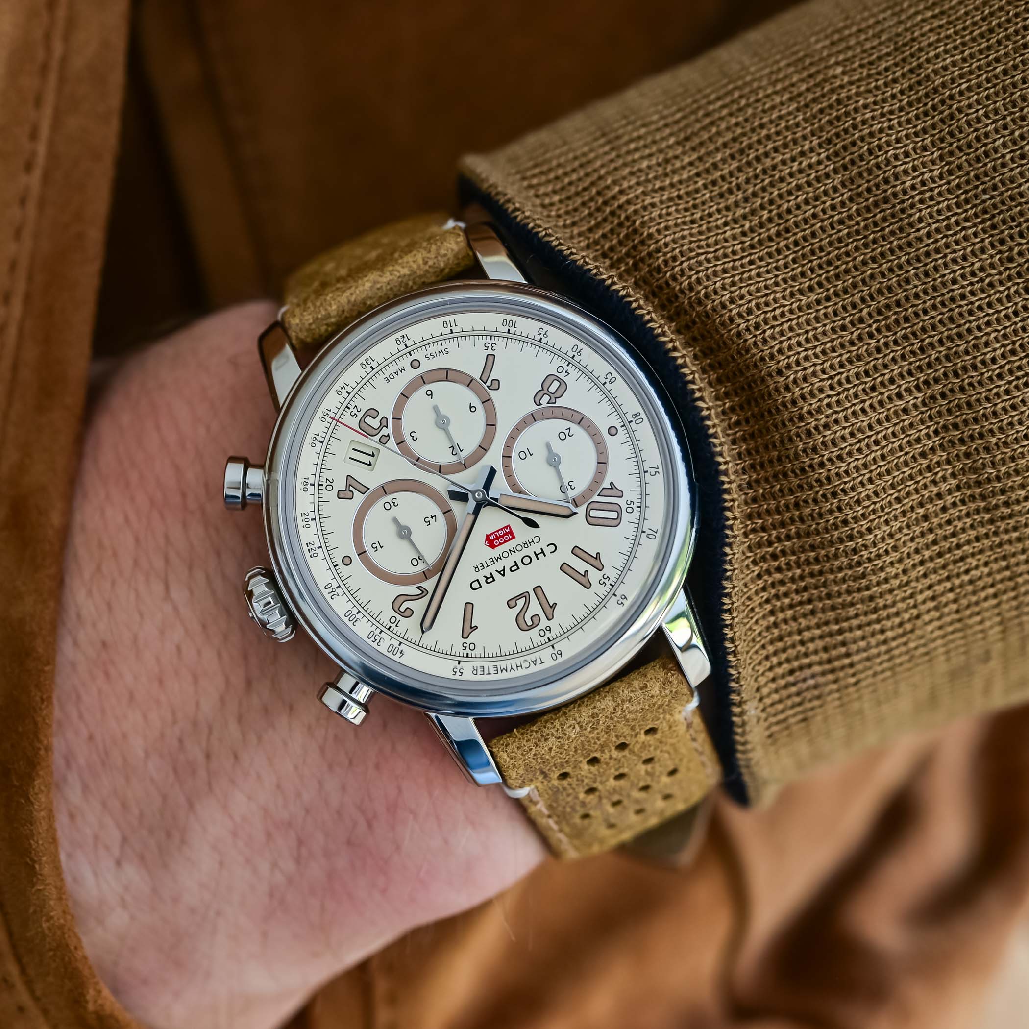 The Raticosa worn on the wrist with a camel knit and suede jacket, the eggshell dial and tan perforated leather racing strap in view