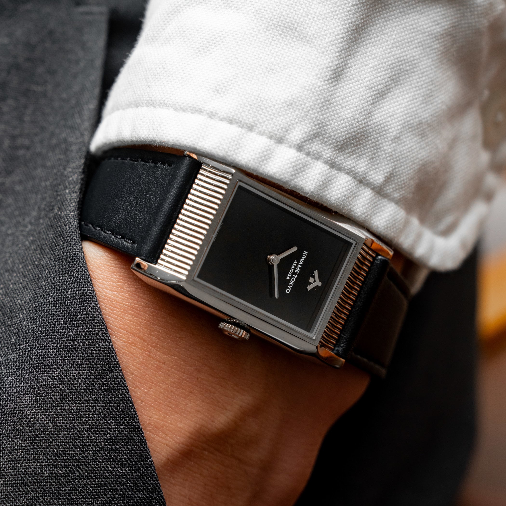 The black-dial Yane worn under a white shirt cuff, showing the rectangular polished steel case, its grooved short ends and the crown at three