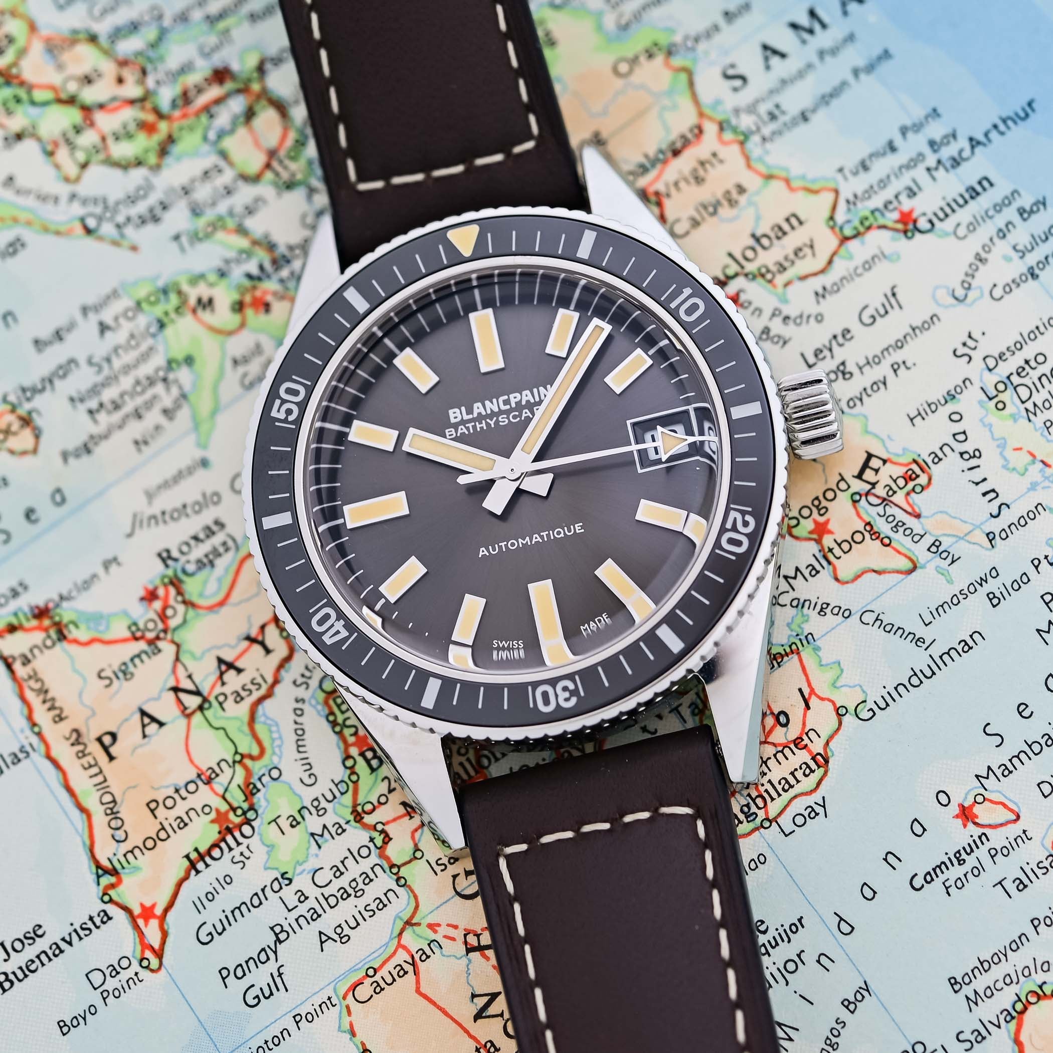 The dial of the Bathyscaphe 70th Anniversary photographed on a vintage map, showing the sunray meteor-grey surface, applied cream-lumed markers, the arrow-tipped seconds hand and the white-framed date at three under Blancpain Bathyscaphe Automatique text