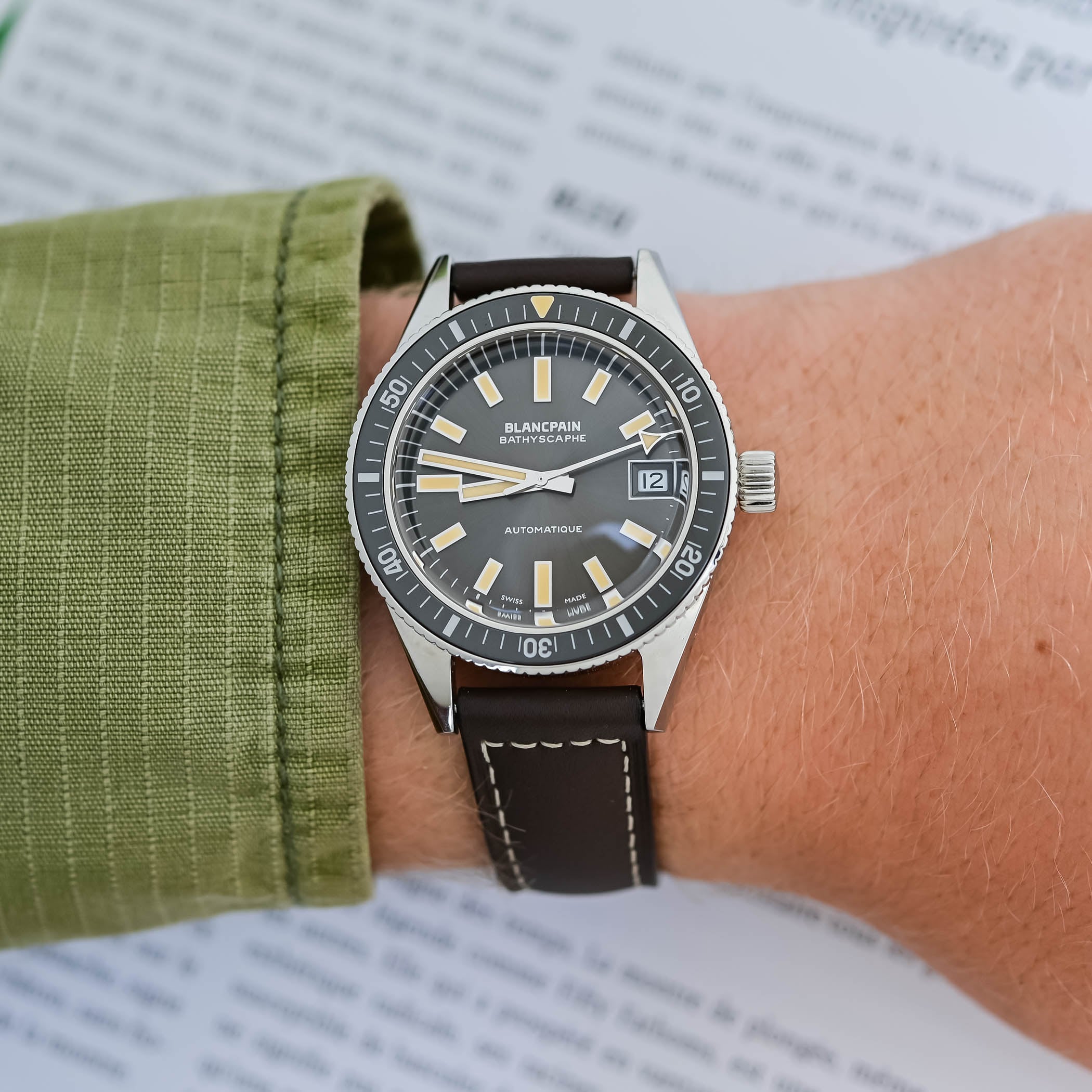 The Bathyscaphe 70th Anniversary worn on the wrist, its 37.4mm polished steel case and black lume-filled bezel shown at an angle with the brown leather strap and off-white stitching