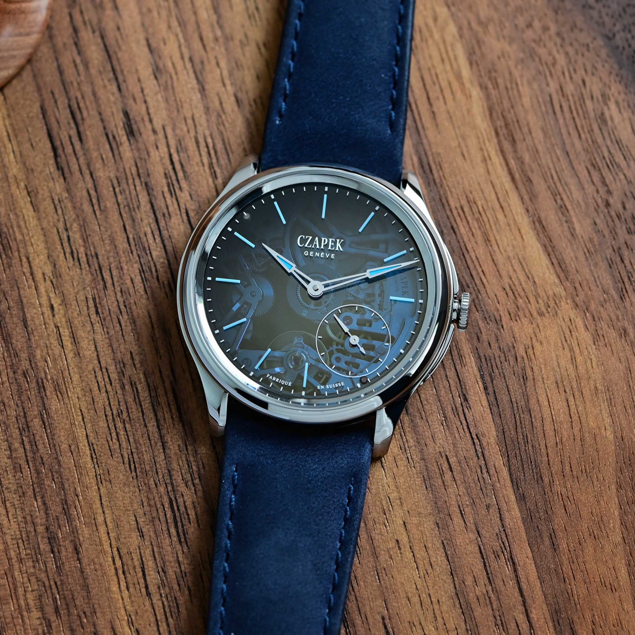 The dial of the Promenade Transparencies Aqua Blue seen straight on, the blue fumé sapphire darkening from a clear centre that shows the gears to an opaque rim, with blue-lumed baton markers, red-tipped hands and a small seconds at 4:30 above Fabriqué en Suisse