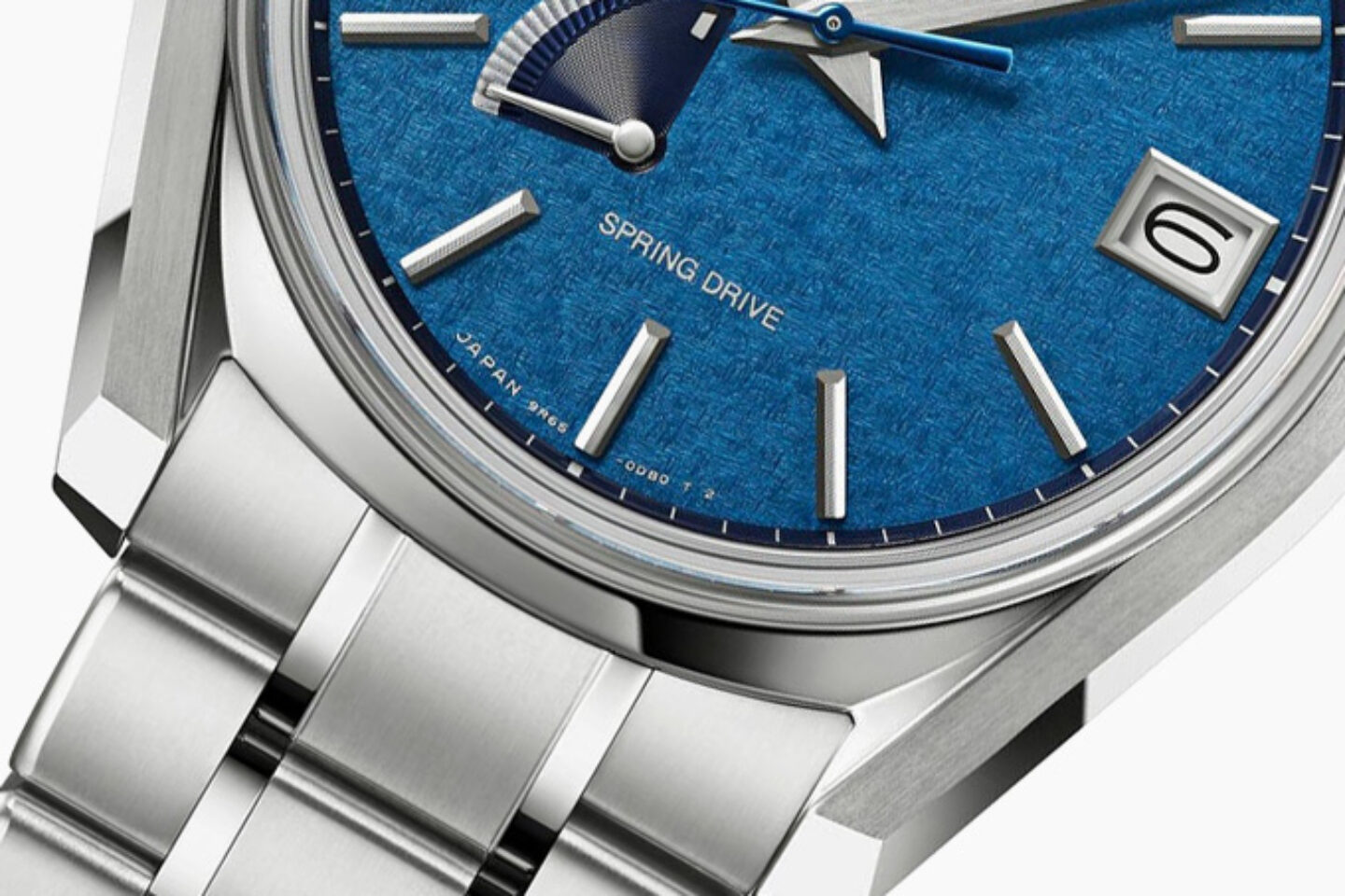 An angled close-up of the SBGA527 showing the Zaratsu-polished titanium case flank and bracelet, the date at three and Spring Drive and Japan 9R65 printed on the blue dial