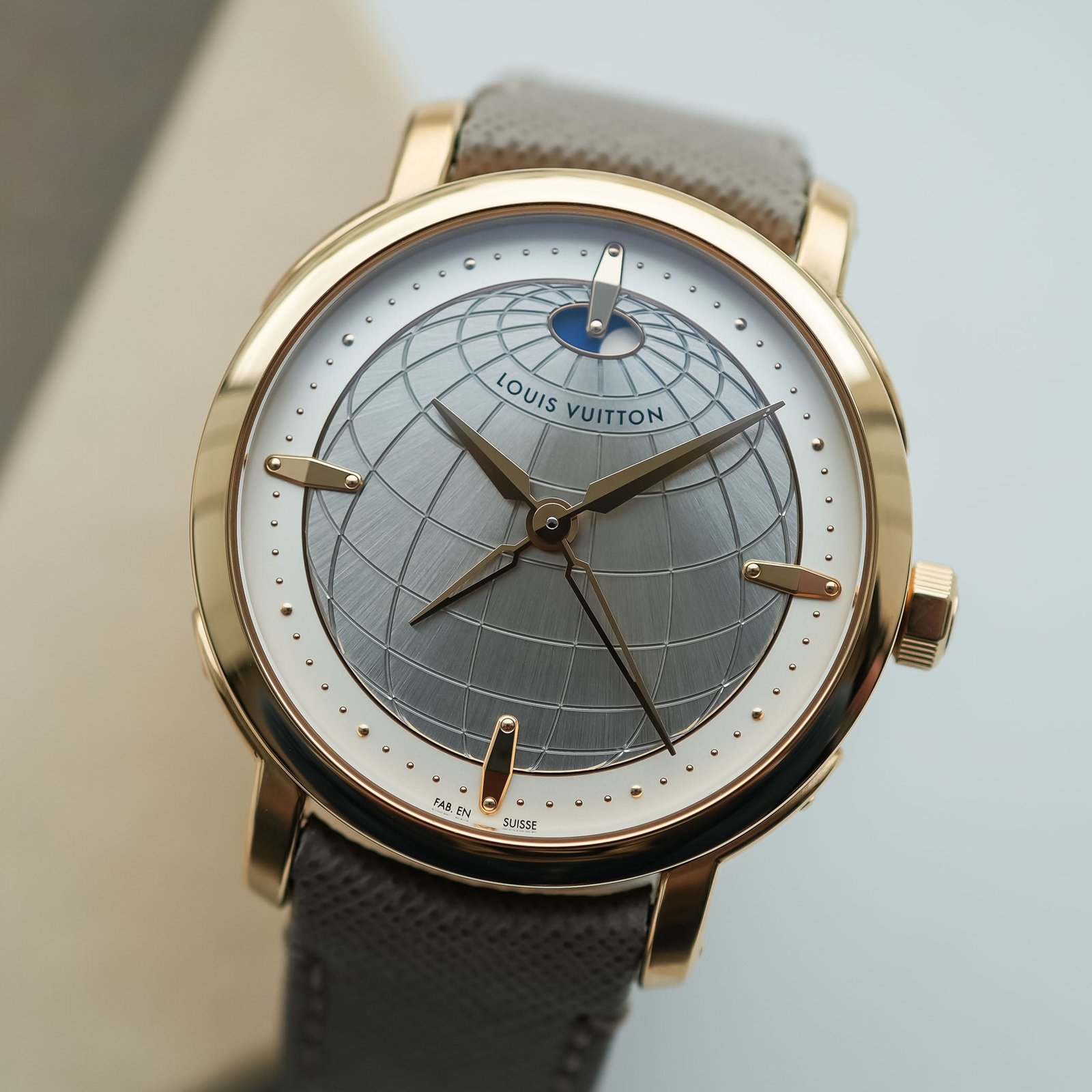 Straight-on view of the Louis Vuitton Escale Twin Zone dial, an engraved globe of latitude and longitude lines with Louis Vuitton across the equator, a blue day/night aperture below twelve and two superimposed sets of gold hands