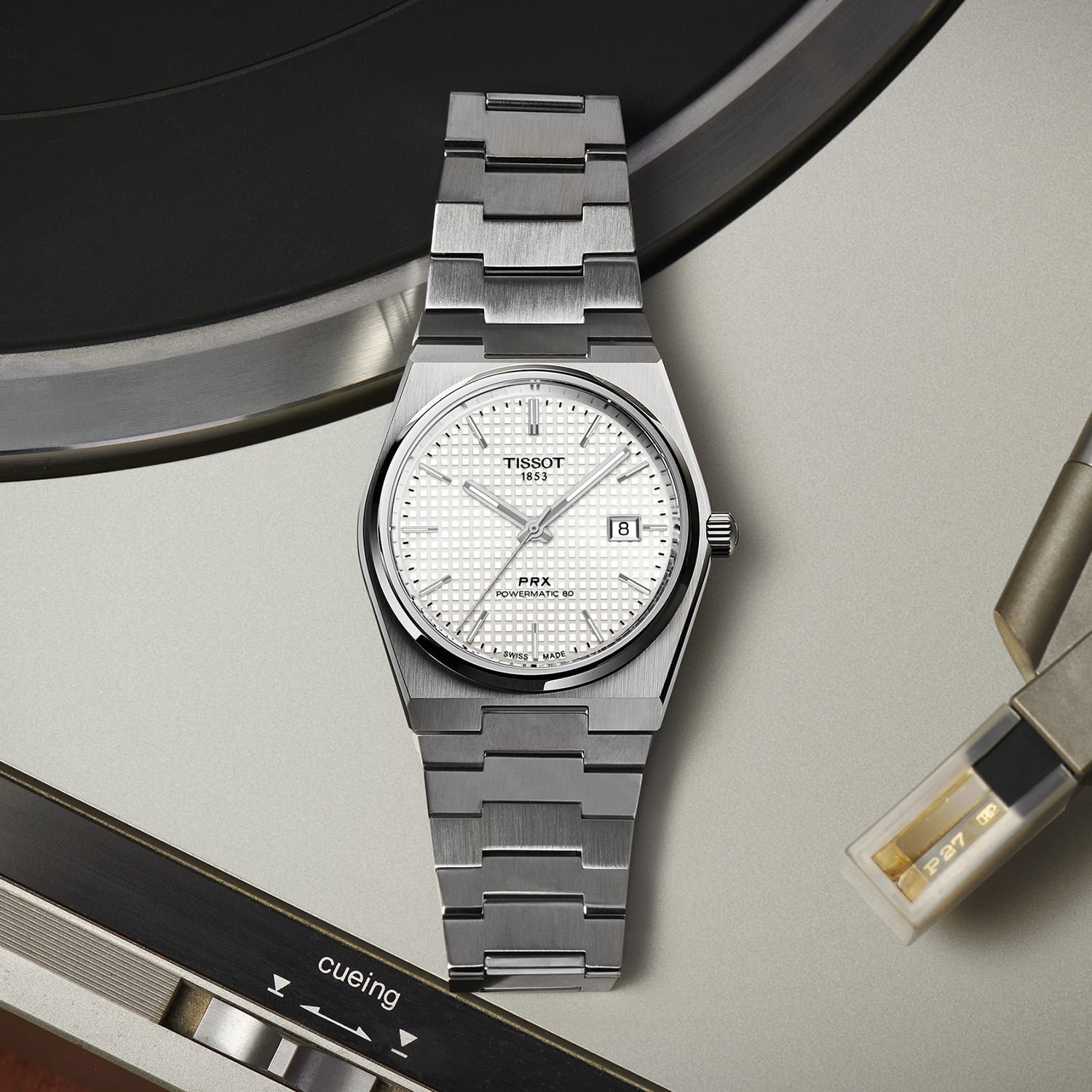 The Tissot PRX 40mm Powermatic 80 mother-of-pearl lying on a turntable platter, three-quarter view showing the white waffle-textured dial, applied markers, framed date at three and the integrated brushed-and-polished steel bracelet