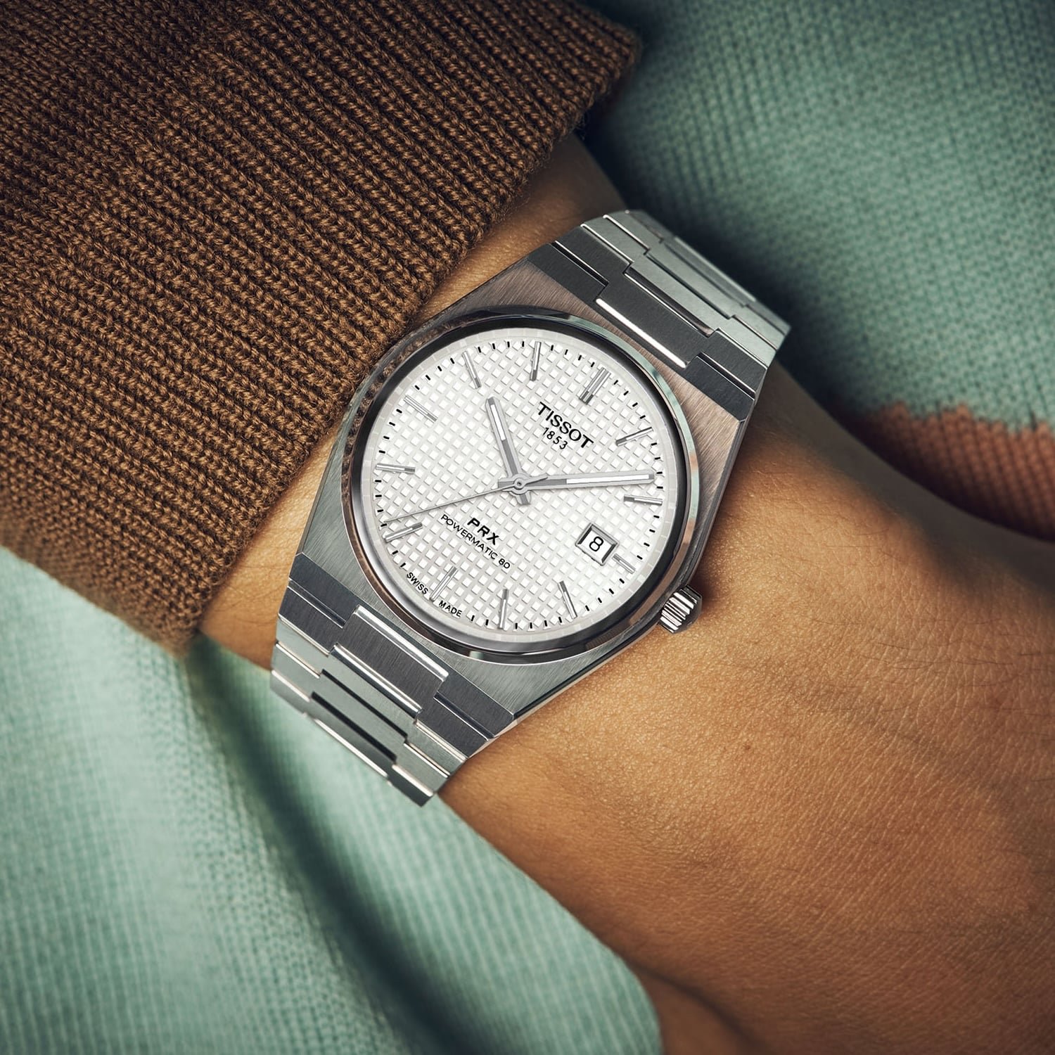 The PRX 40mm mother-of-pearl worn on the wrist beside brown and mint knitwear, the iridescent white dial and integrated steel bracelet catching daylight