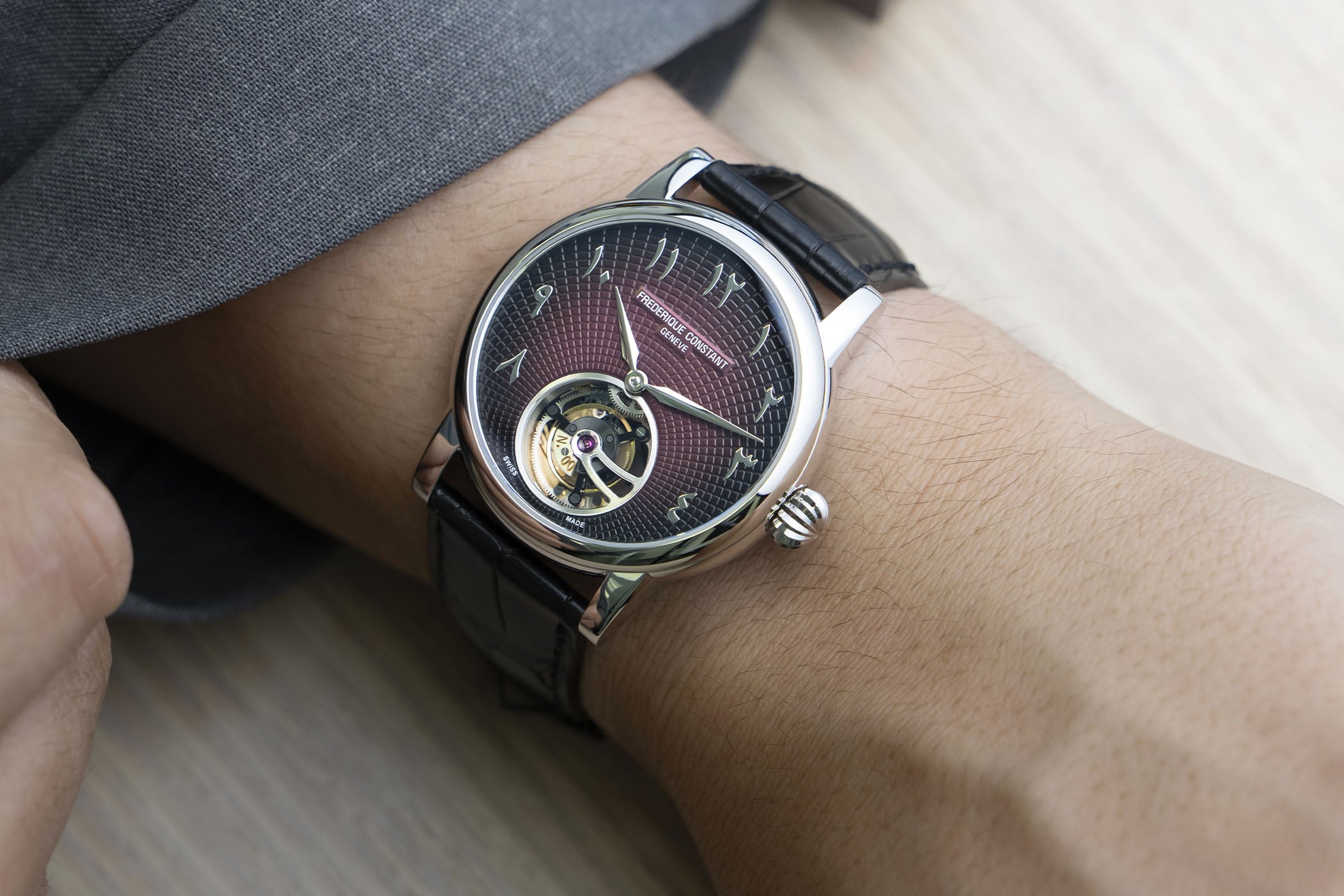 The platinum Frederique Constant Tourbillon Julie worn on the wrist under a grey suit cuff, its burgundy-to-black guilloché dial and six-o'clock tourbillon catching the light