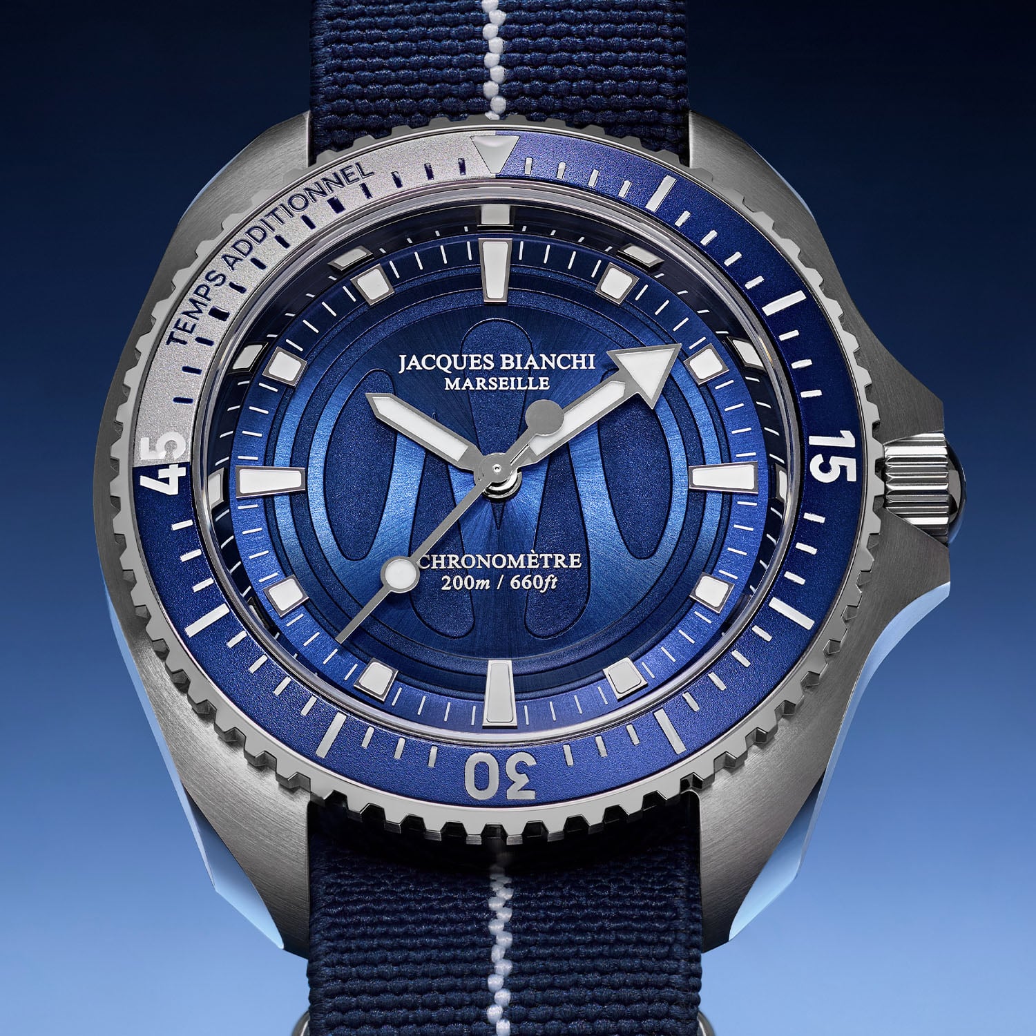 Macro of the Jacques Bianchi OM200 deep-blue sunburst dial, the Olympique de Marseille monogram embossed at the centre, applied luminous markers, TEMPS ADDITIONNEL on the steel bezel and CHRONOMÈTRE 200m/660ft above six