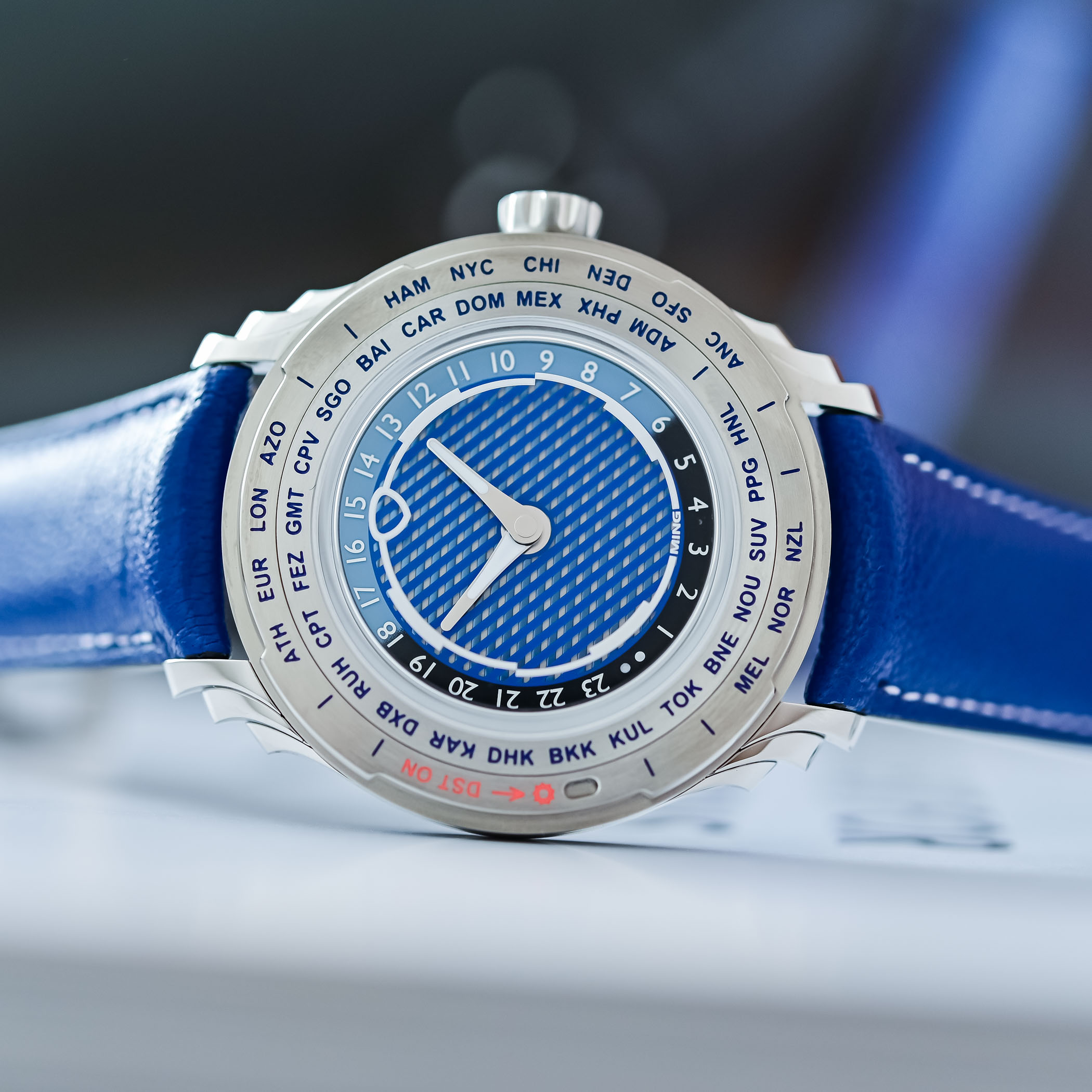 The Ming 57.05 Comet in profile on its cobalt-blue Jean Rousseau leather strap, showing the triple-stepped lugs, the knurled crown and the DST ON aperture set into the chapter ring