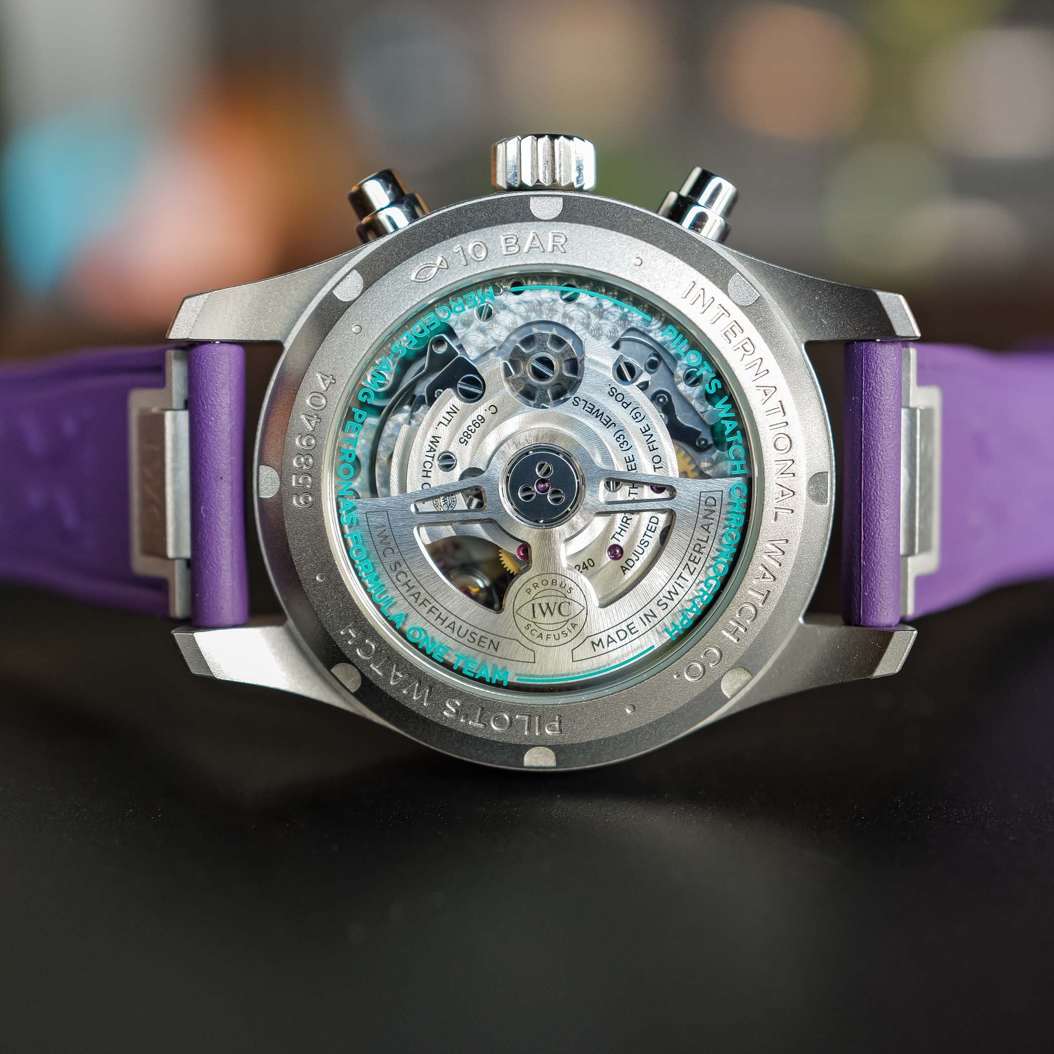 The titanium caseback of the IWC IW388121 showing calibre 69385 through sapphire, the openworked rotor and engravings reading Pilot's Watch Chronograph, Mercedes-AMG PETRONAS Formula One Team and 10 bar in teal-green