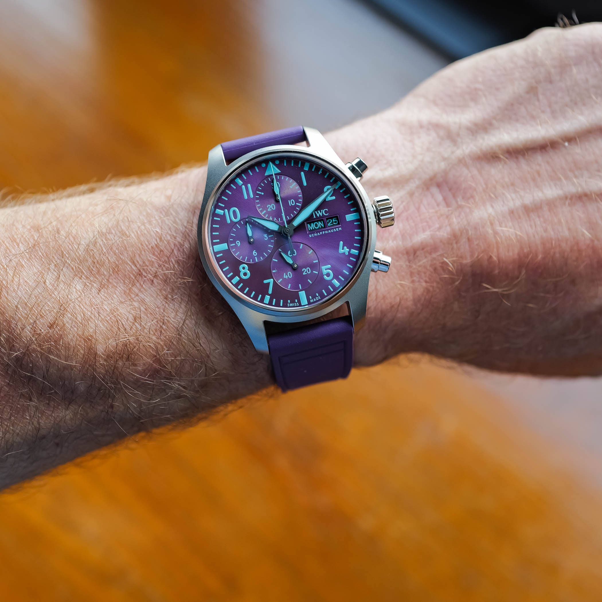 The IWC IW388121 worn on the wrist, its purple sunburst dial and teal-green markers catching daylight, titanium case and purple rubber strap