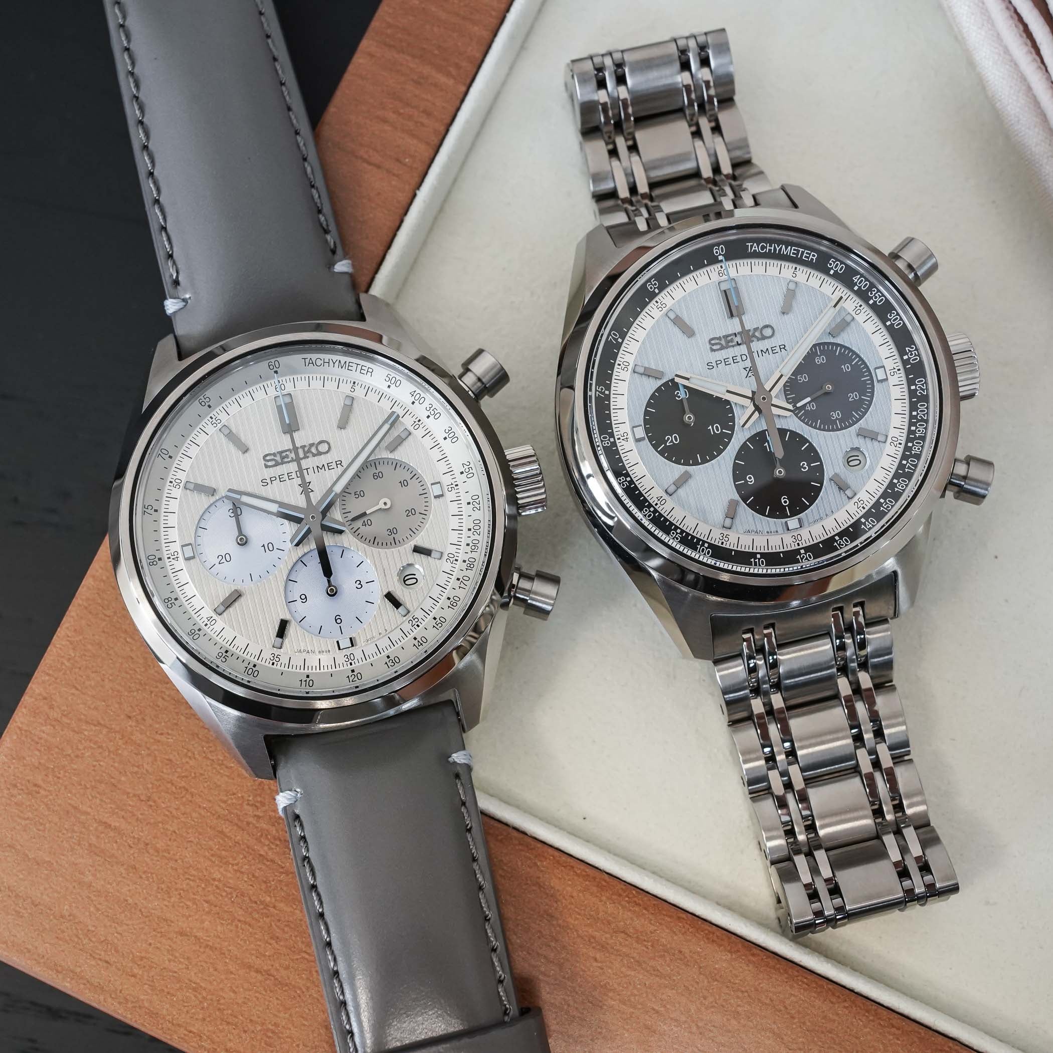 The two Seiko Speedtimer chronographs, the silver-dial HBD002 on grey leather and the panda-style HBD001 with black counters on a steel bracelet, showing the tachymeter bezels and three registers