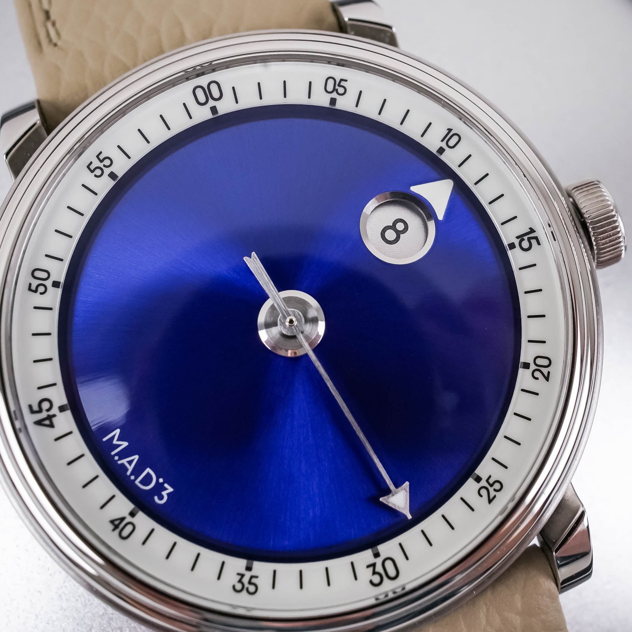 The M.A.D.3 blue sunray dial in close-up, the circular jumping-hour window showing 8 and the arrow-shaped central seconds hand crossing the peripheral minute track