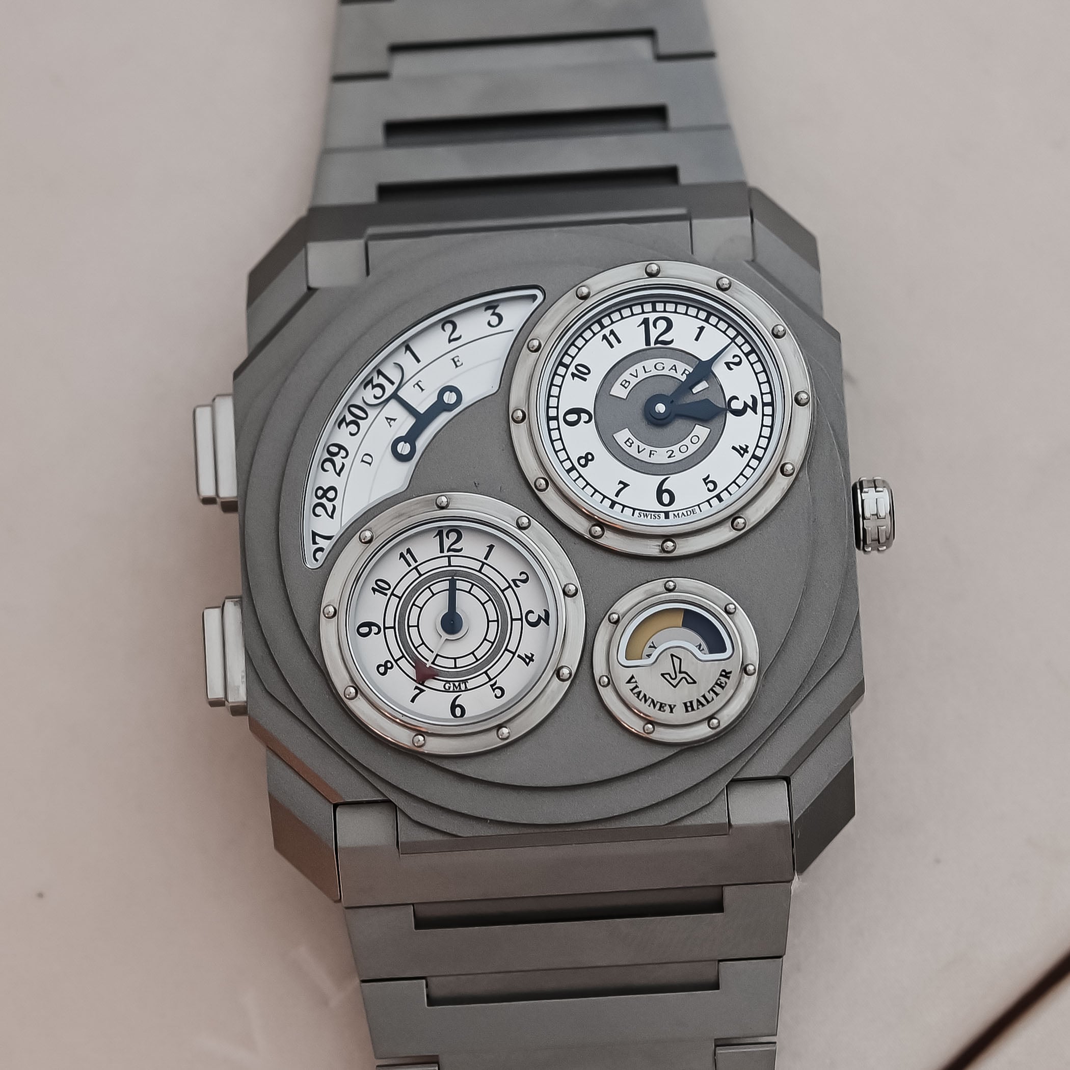 A macro of the titanium dial showing the four opaline sub-dials, the retrograde date arc marked DATE, the local-time dial marked BVLGARI and BVF 200, the concentric GMT and running-seconds display with its red arrow hand, and the day/night indicator under the Vianney Halter signature
