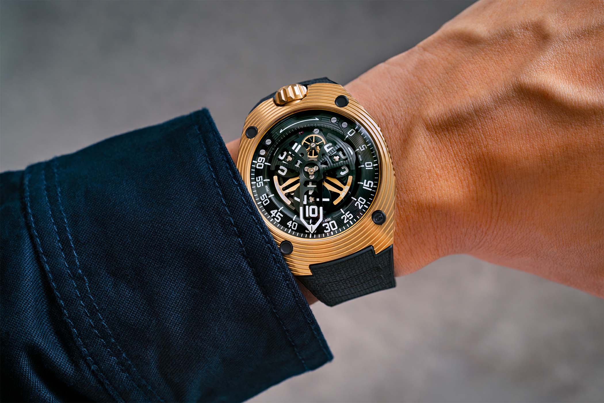 The yellow-gold UR-150 Golden Scorpion worn on a wrist on a black textured rubber strap, the fluted crown at twelve and the satellite display under a domed sapphire crystal