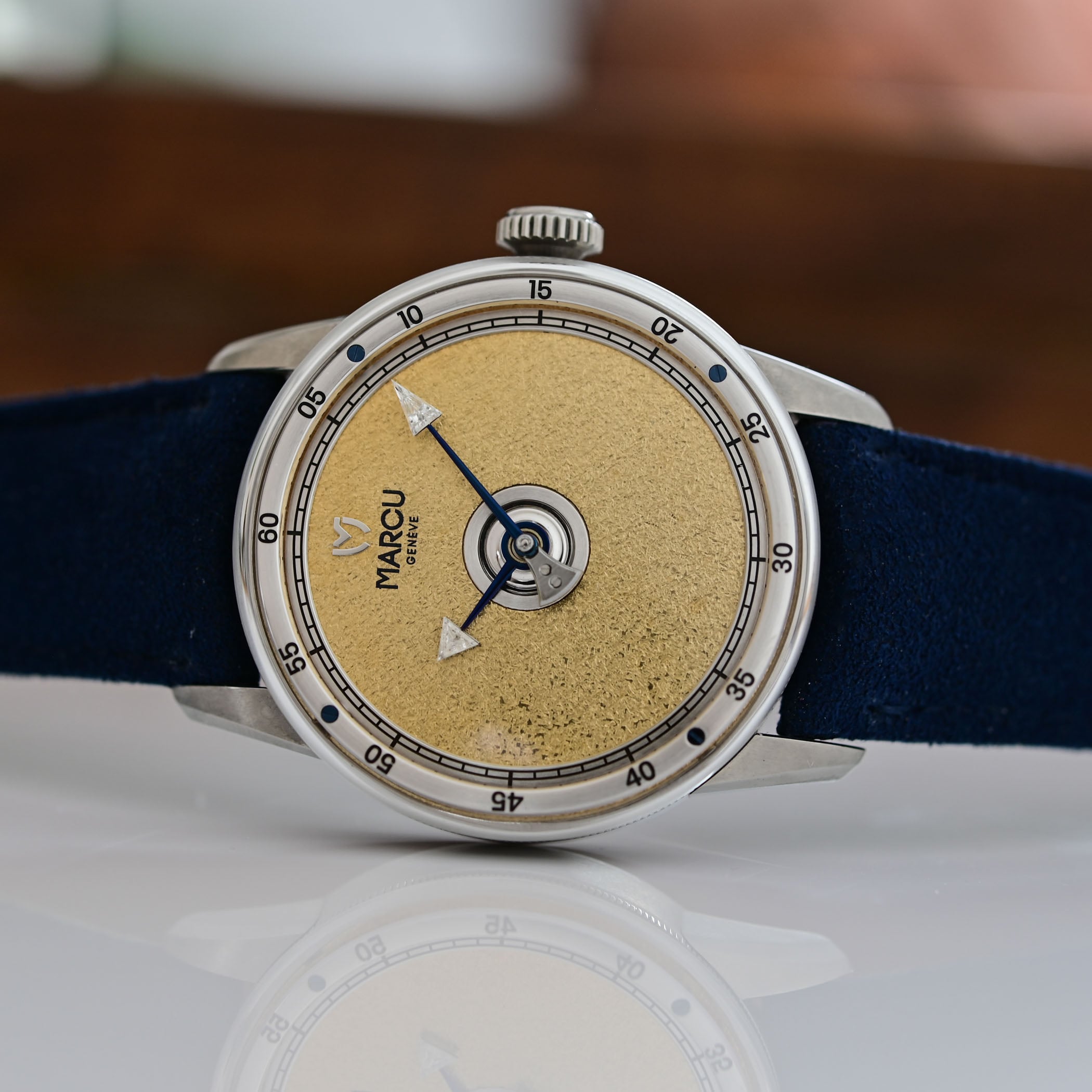 The golden-dial version of the Marcu Initial in profile, showing the blued steel hands tipped with triangle-cut diamonds and the domed crystal meeting the case band, on a blue Alcantara strap