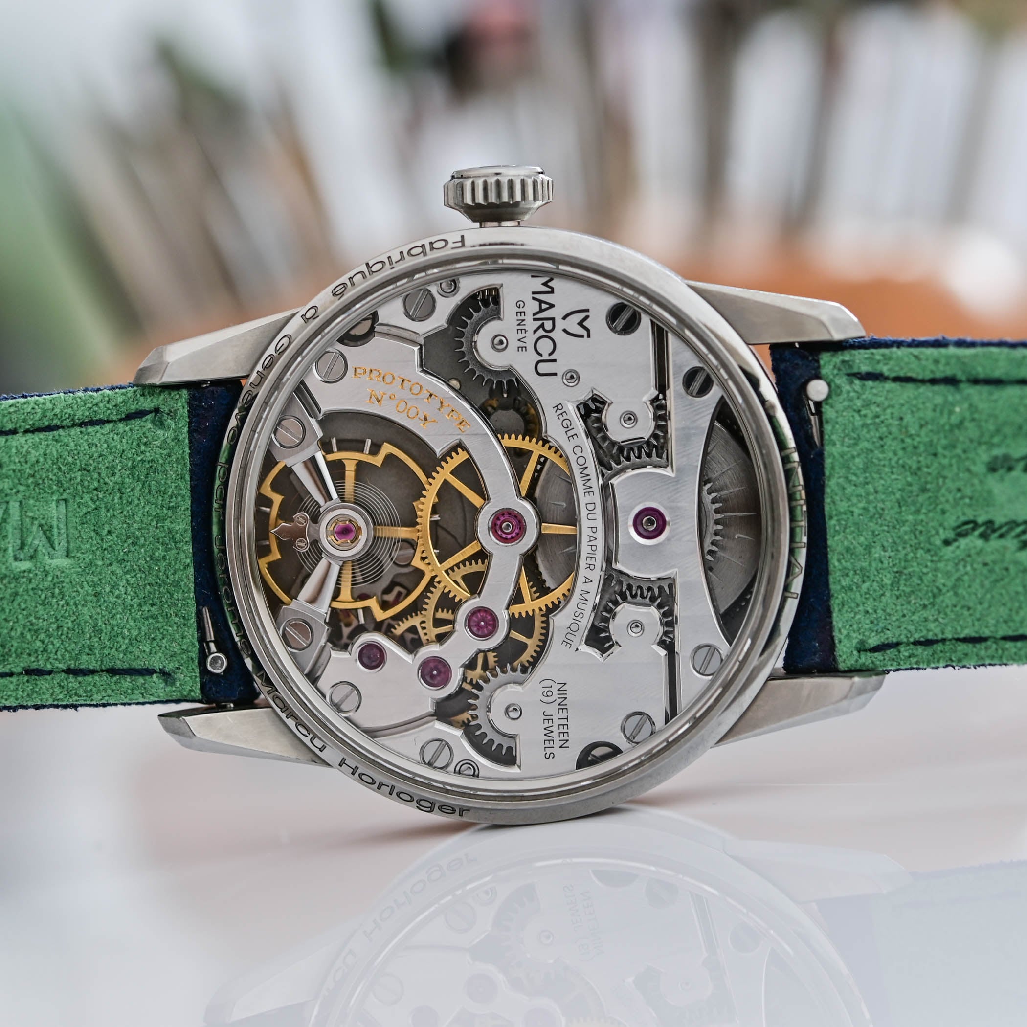Caseback view of the hand-wound JM01 calibre through sapphire, its symmetrical bridges engraved MARCU GENEVE, NINETEEN 19 JEWELS and réglé comme du papier à musique
