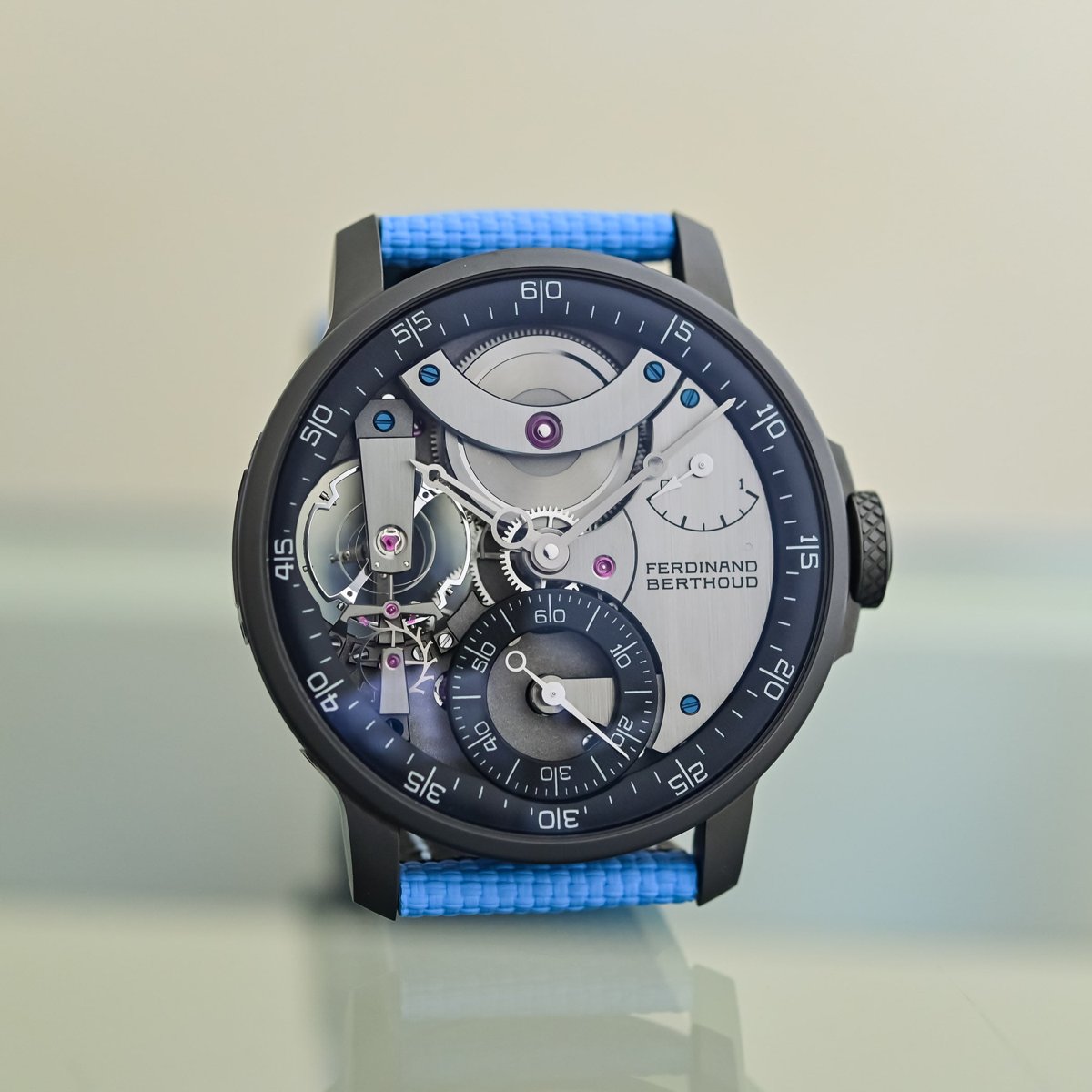The dial side of the FB 3SPC.4-1, its black ceramised titanium case and dark dial with a peripheral hours-and-minutes ring, small seconds at six and the cylindrical balance exposed at nine, on a light-blue textile strap