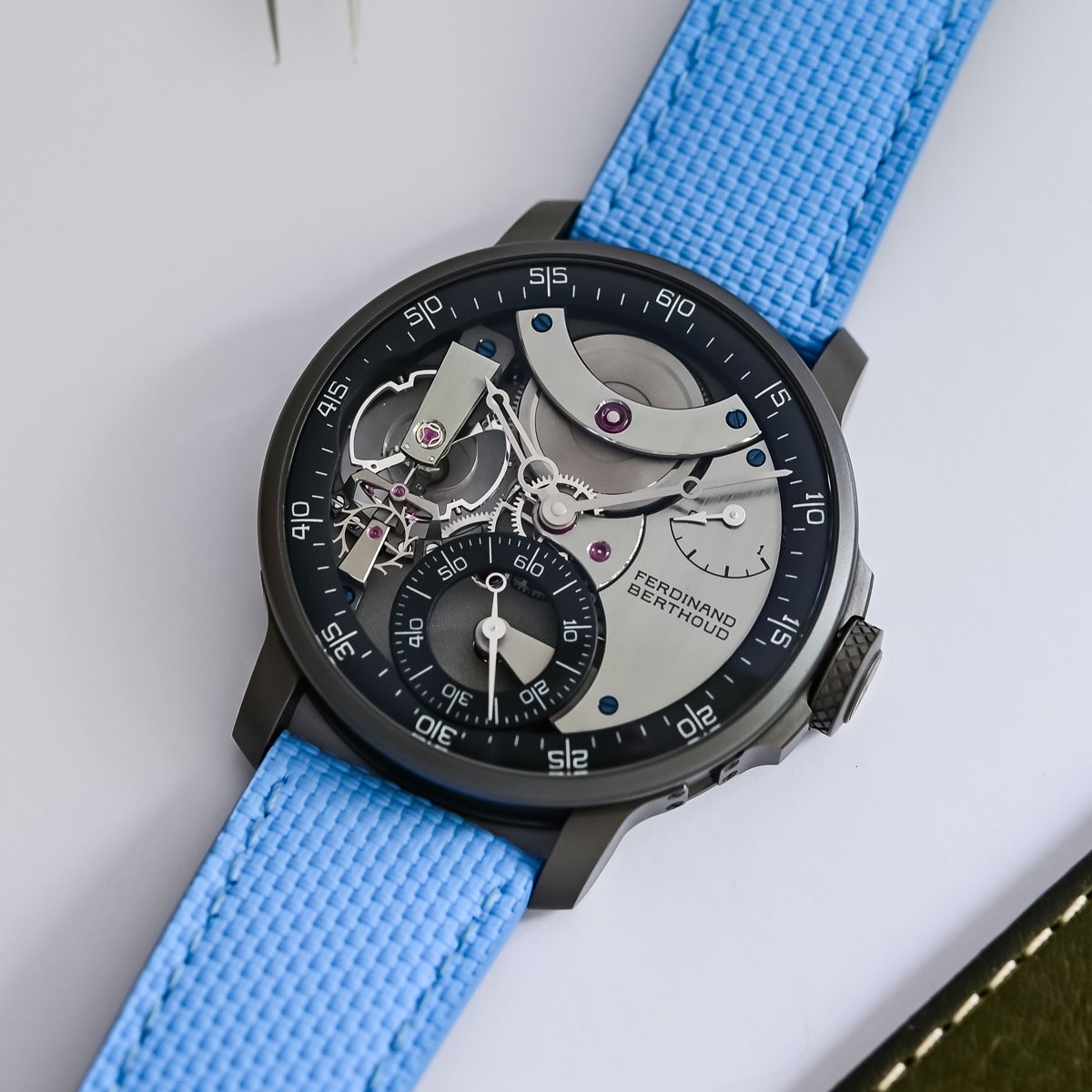 The FB 3SPC.4-1 at a three-quarter angle, the black ceramised titanium case with crown guards beside the large crown and the power-reserve bridge on the dark dial, on a light-blue textile strap