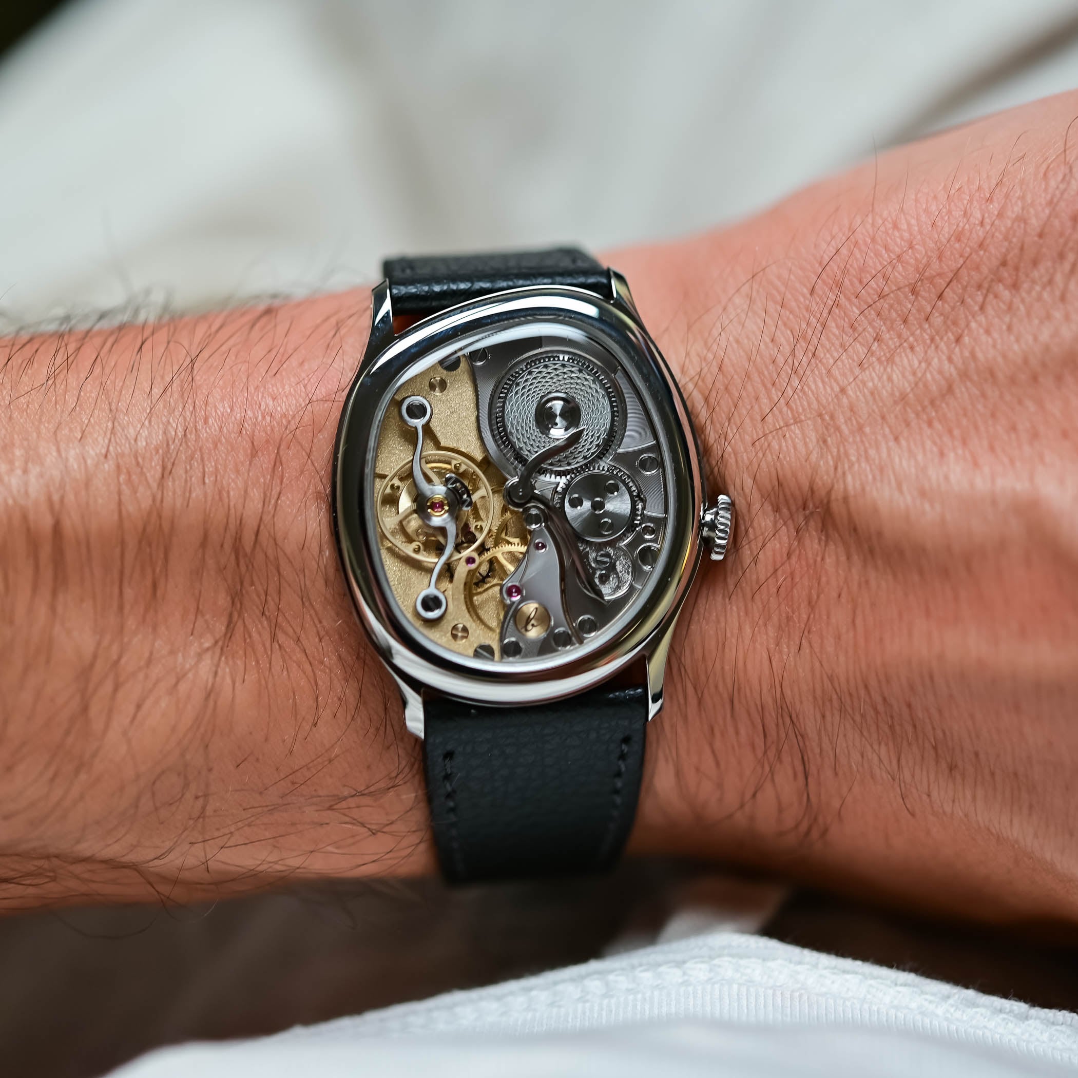 The white gold Mirage 38 Miroir on a black strap on the wrist, the asymmetric case framing the exposed movement that serves as the dial