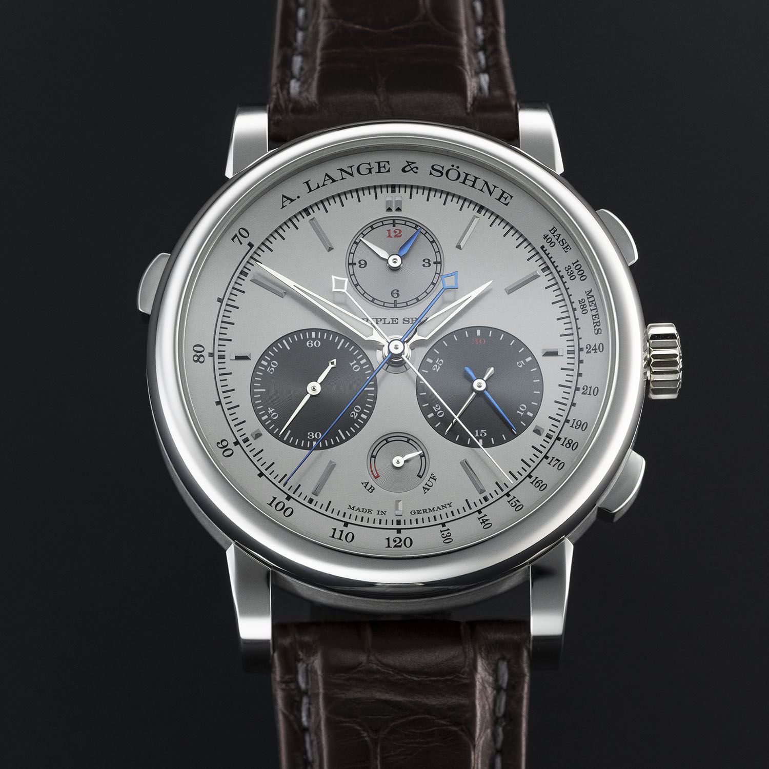The platinum Triple Split seen straight on, the rhodium-coloured silver dial with grey subdials at twelve, four and eight, a blued rattrapante hand, the Ab Auf power reserve at six and a tachymeter scale on the flange