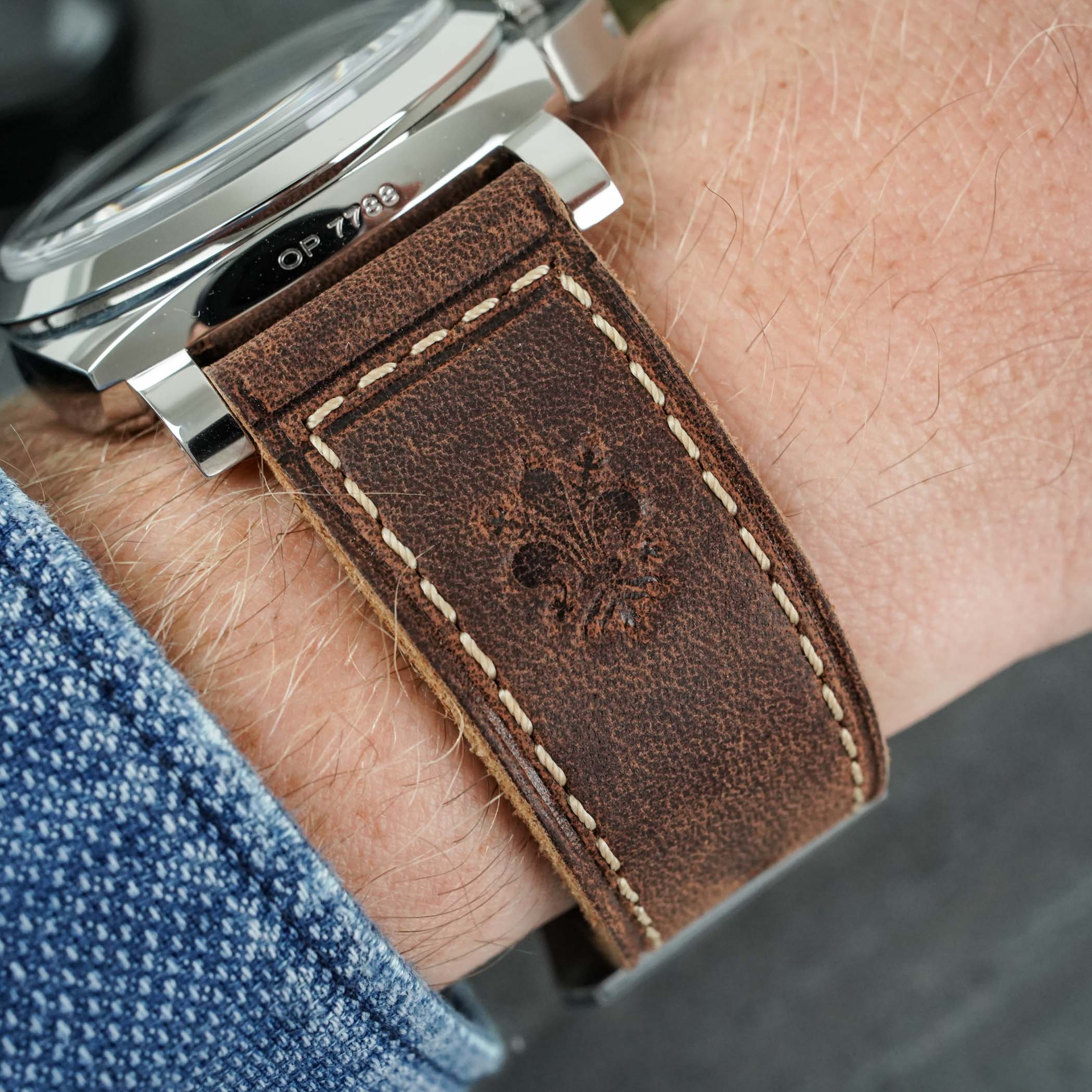 A wrist shot of the steel PAM01794 showing the brown Tuscan calf strap embossed with the Florentine lily and the case flank engraved OP 7788