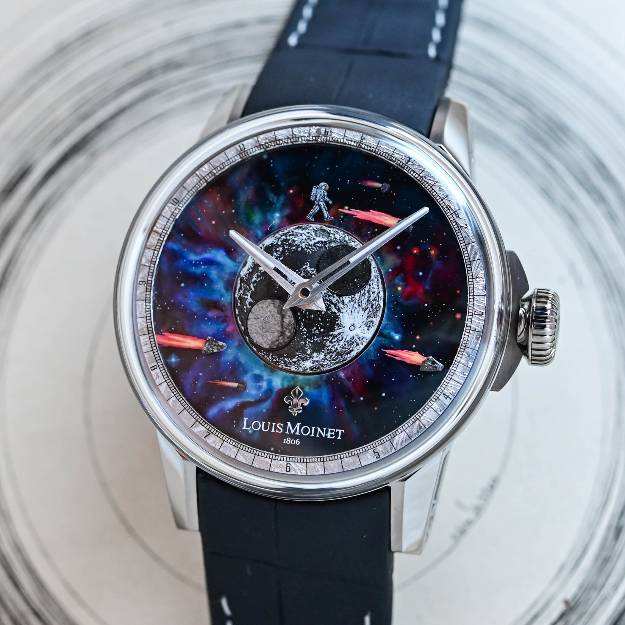 Top-down view of the Louis Moinet Moon Meteor dial, a domed lunar disc set with two grey lunar meteorite discs, a hand-painted astronaut and orange comets over a painted nebula, framed by a Muonionalusta meteorite flange