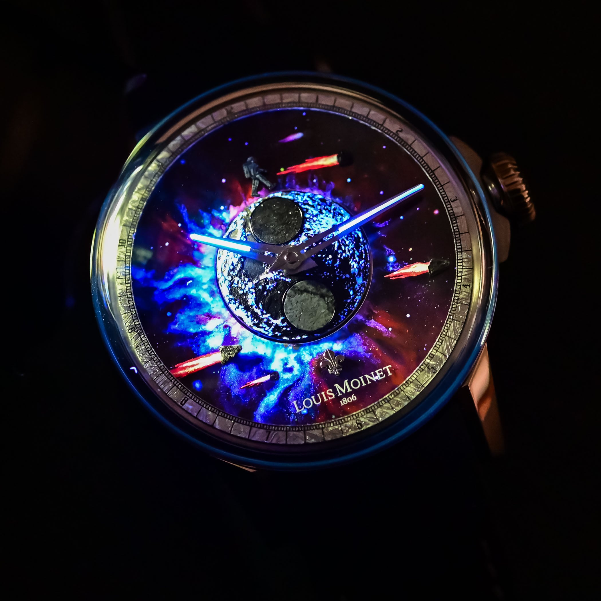 The same dial photographed in the dark, luminescent paint glowing blue and violet to reveal a second celestial composition