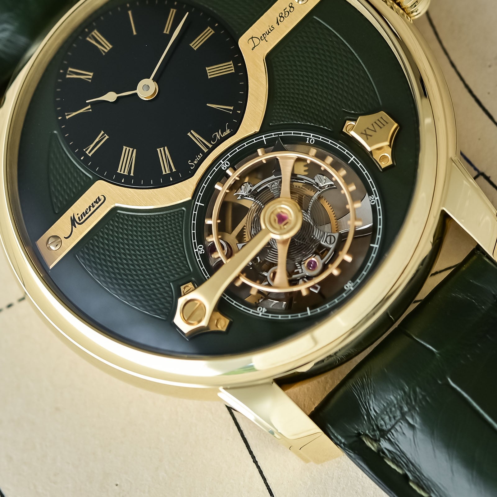 A macro of the Minerva 137548 dial showing the exposed tourbillon, the large screw balance and the gold cage bridge over an olive-green ground engraved Minerva Depuis 1858